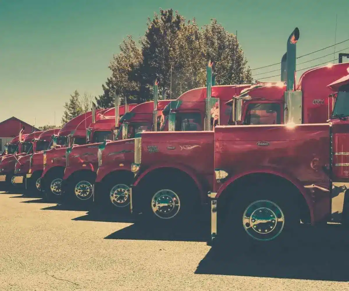 Row of red semi-trucks parked in a lot under clear sky.
