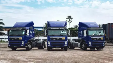 Three blue Volvo trucks parked side by side in a lot.