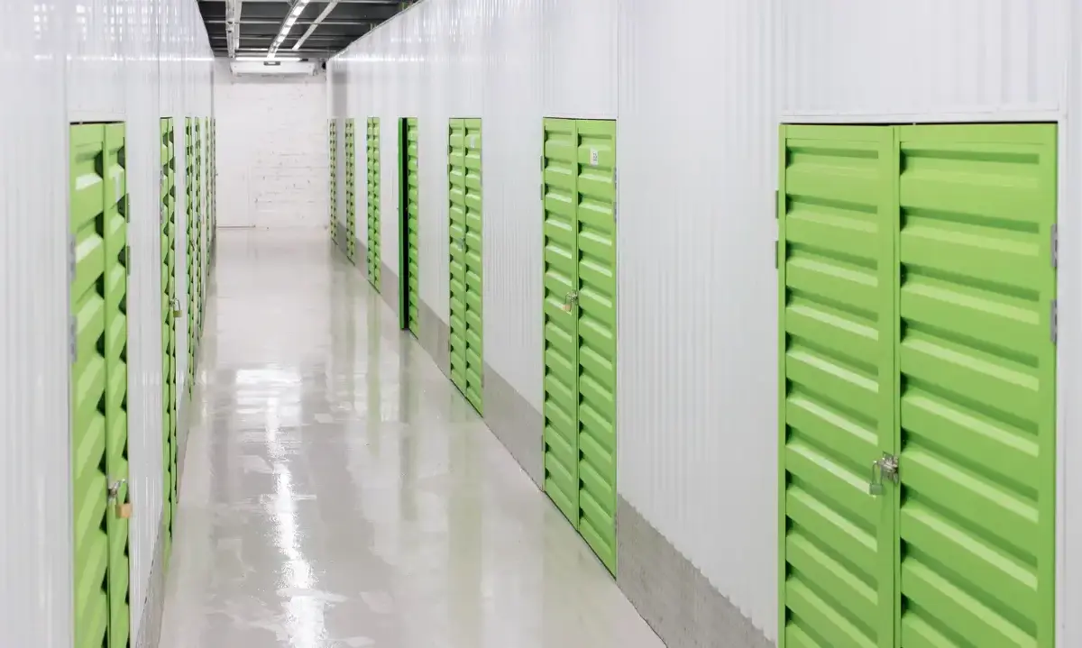 Indoor self-storage corridor with rows of lime-green unit doors, glossy floor, and overhead lights.