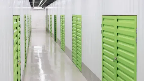 Indoor self-storage corridor with rows of lime-green unit doors, glossy floor, and overhead lights.