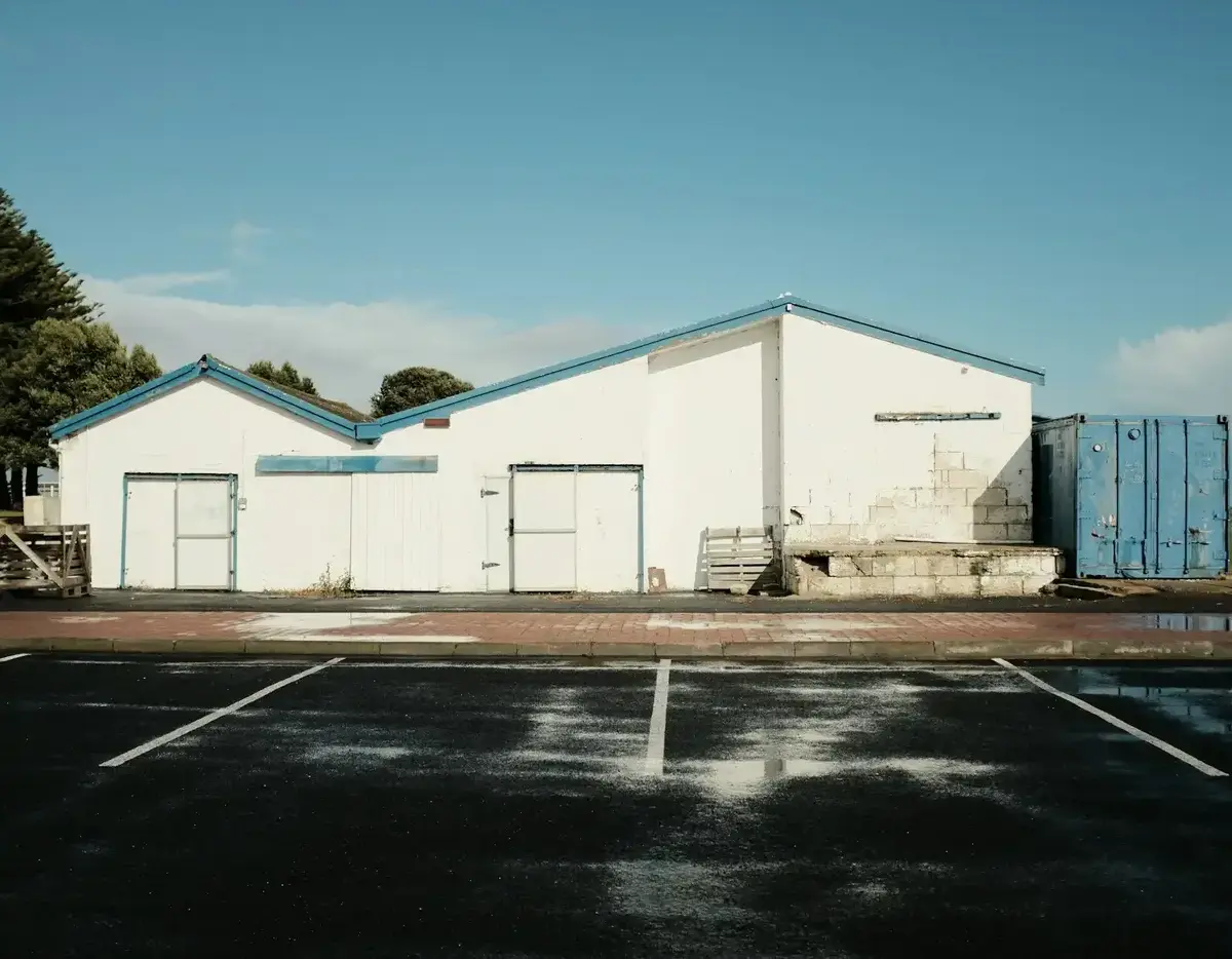 White industrial building next to an empty parking lot under a clear sky.