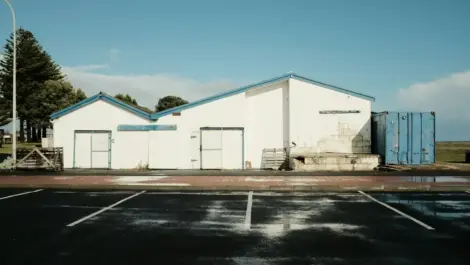 White industrial building next to an empty parking lot under a clear sky.