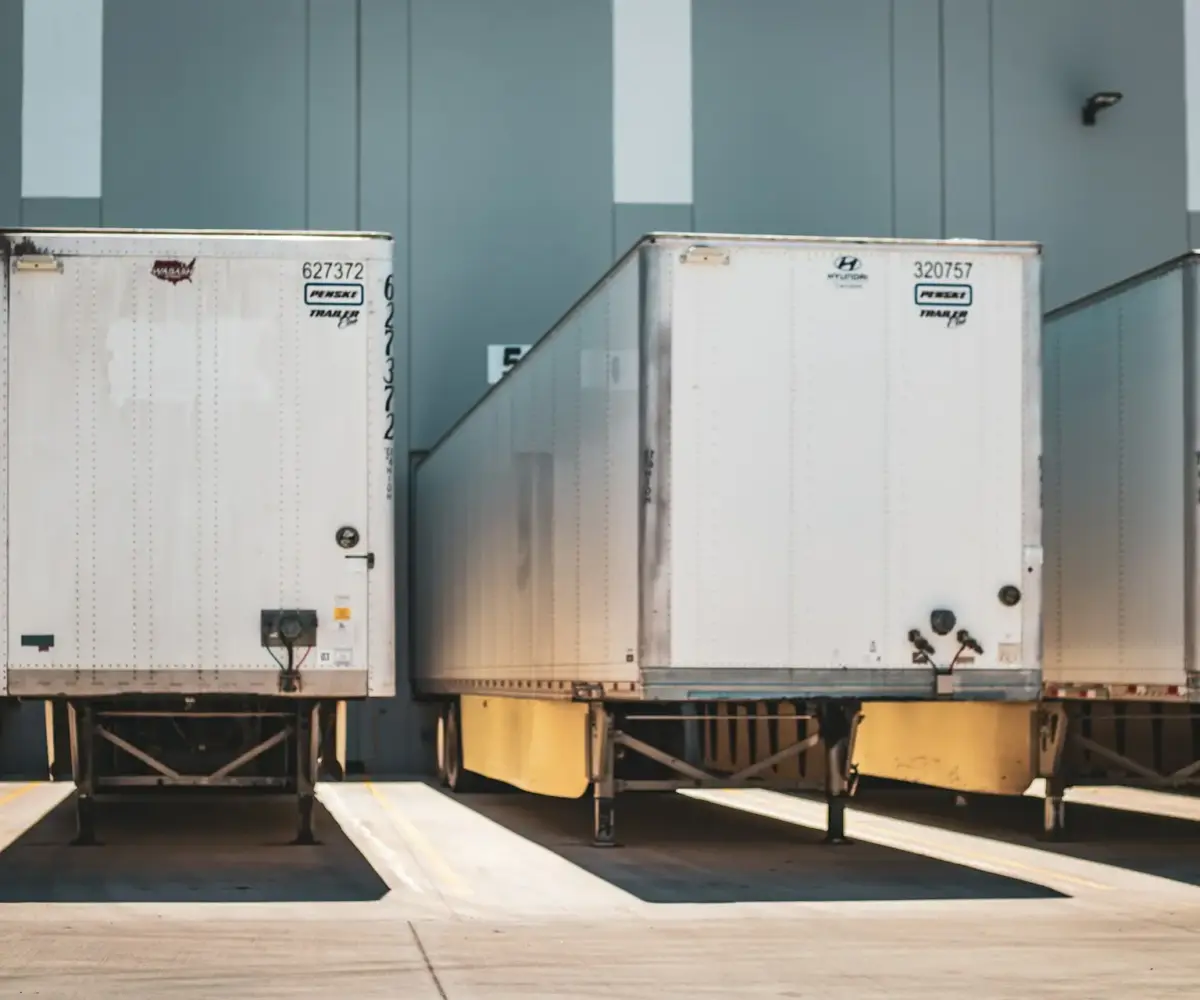 Row of white semi-trailers parked at a loading dock in an industrial facility.