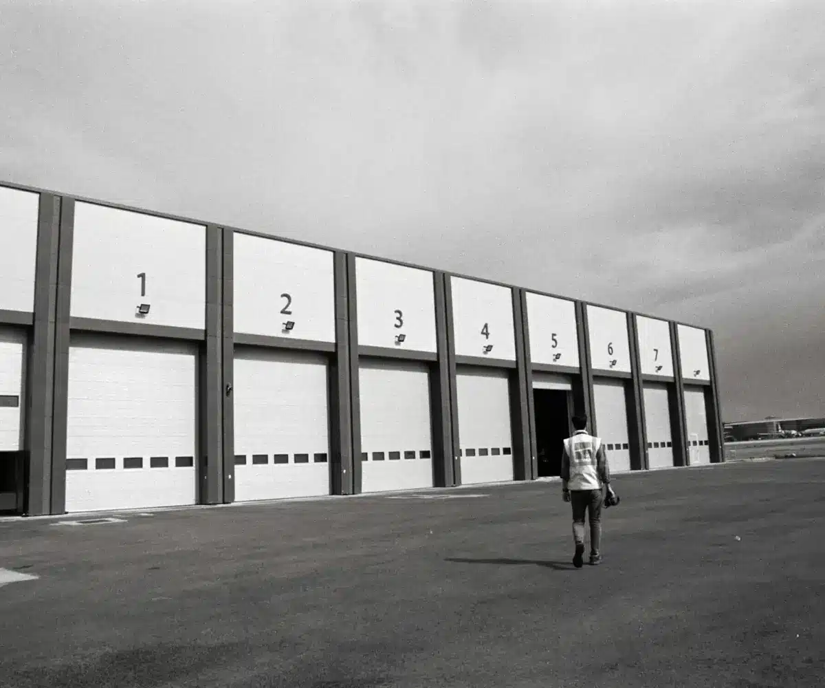 A person walking toward large numbered storage bay doors at an industrial outdoor facility.