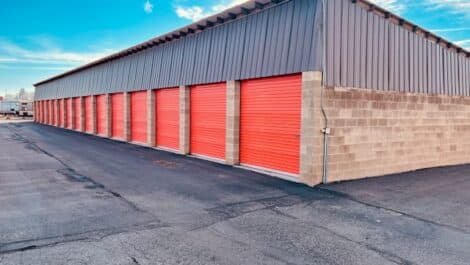 Outdoor self-storage facility with red roll-up doors and asphalt driveway.
