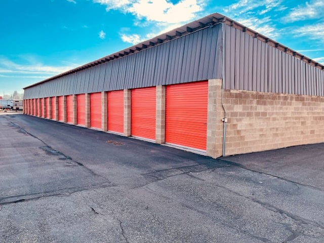 Outdoor self-storage facility with red roll-up doors and asphalt driveway.