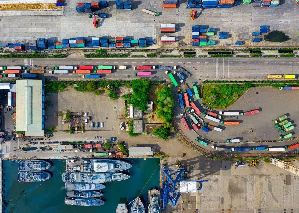 Aerial view of a busy port with ships, trucks, and containers in outdoor storage areas.