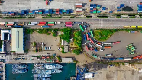 Aerial view of a busy port with ships, trucks, and containers in outdoor storage areas.