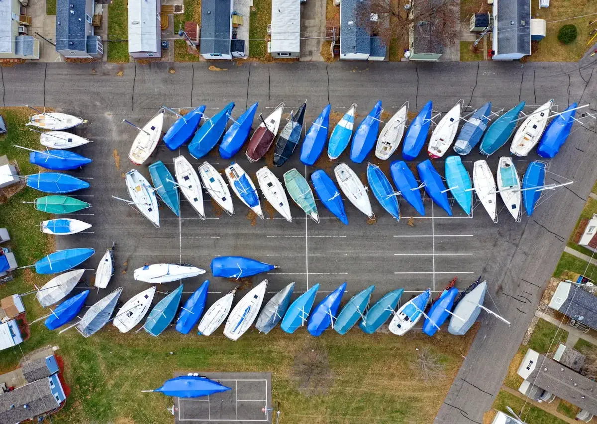 Aerial view of sailboats in a storage lot, many covered with blue tarps.