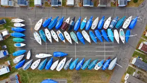Aerial view of sailboats in a storage lot, many covered with blue tarps.