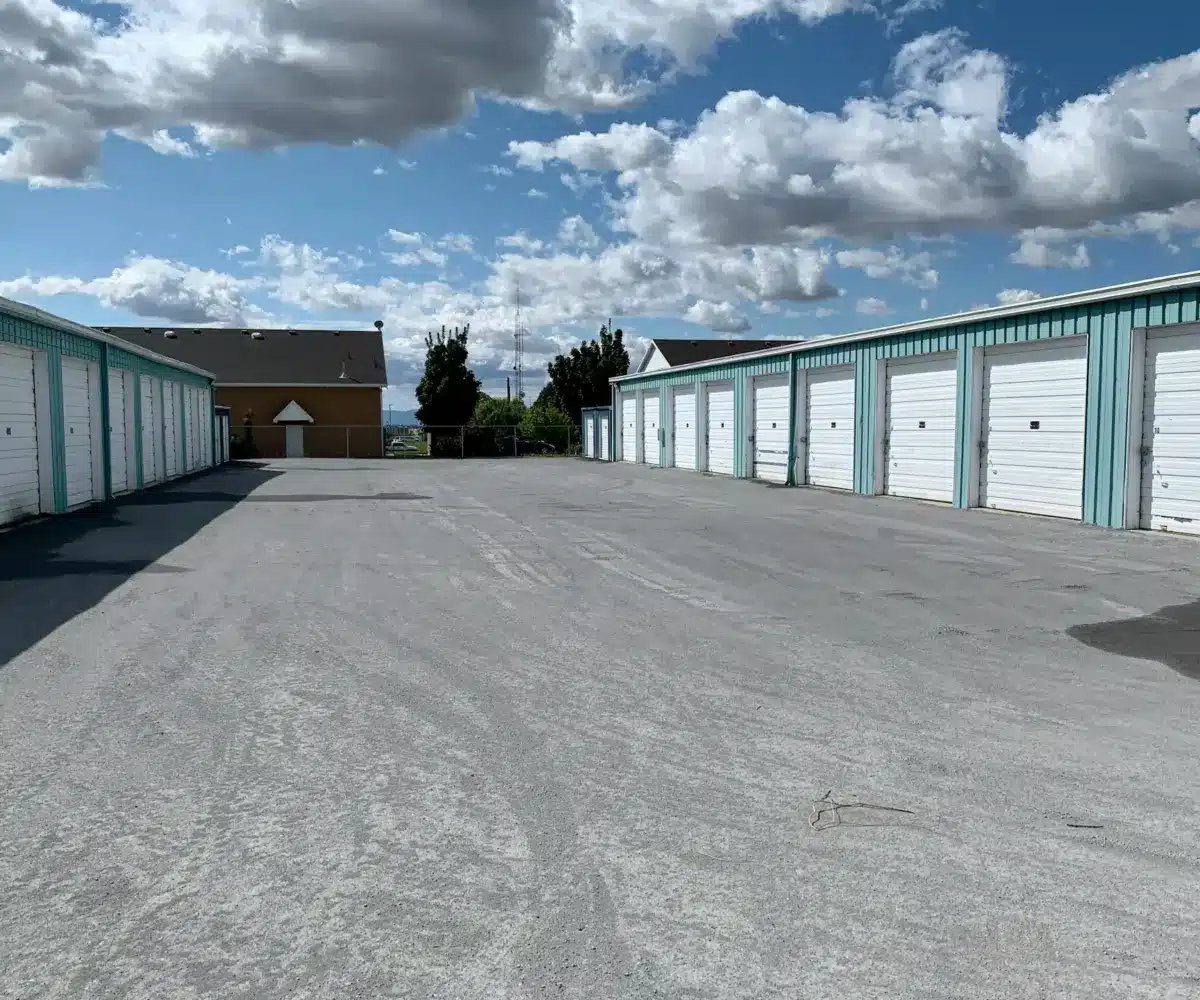 Outdoor self-storage units with white roll-up doors under a partly cloudy sky.