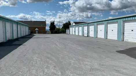 Outdoor self-storage units with white roll-up doors under a partly cloudy sky.
