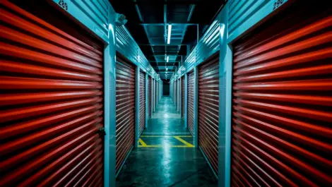 Dimly lit hallway of indoor storage units with red roll-up doors.