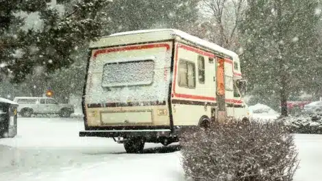 Camper van covered in snow during winter storm in a residential lot.