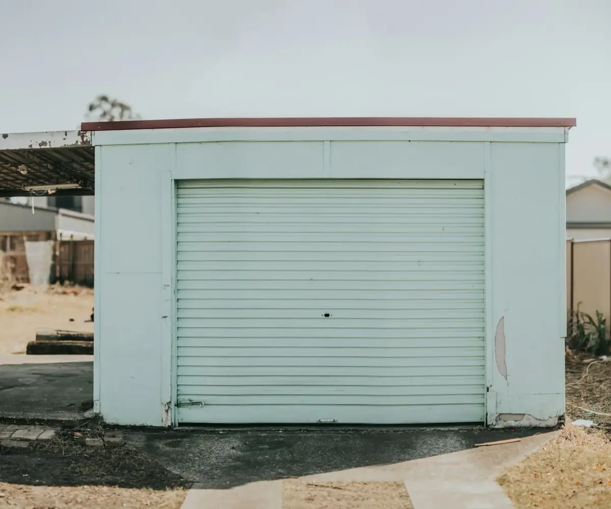 Small pale-blue storage garage with a closed roll-up door.