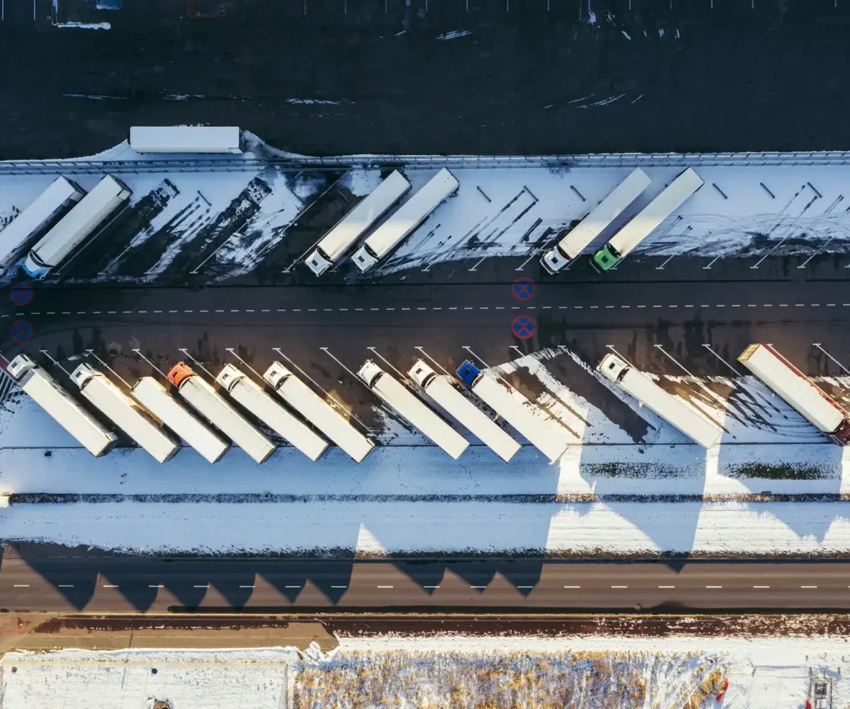 Aerial view of trucks parked in a snow-covered commercial truck parking lot.