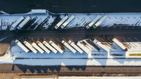 Aerial view of trucks parked in a snow-covered commercial truck parking lot.