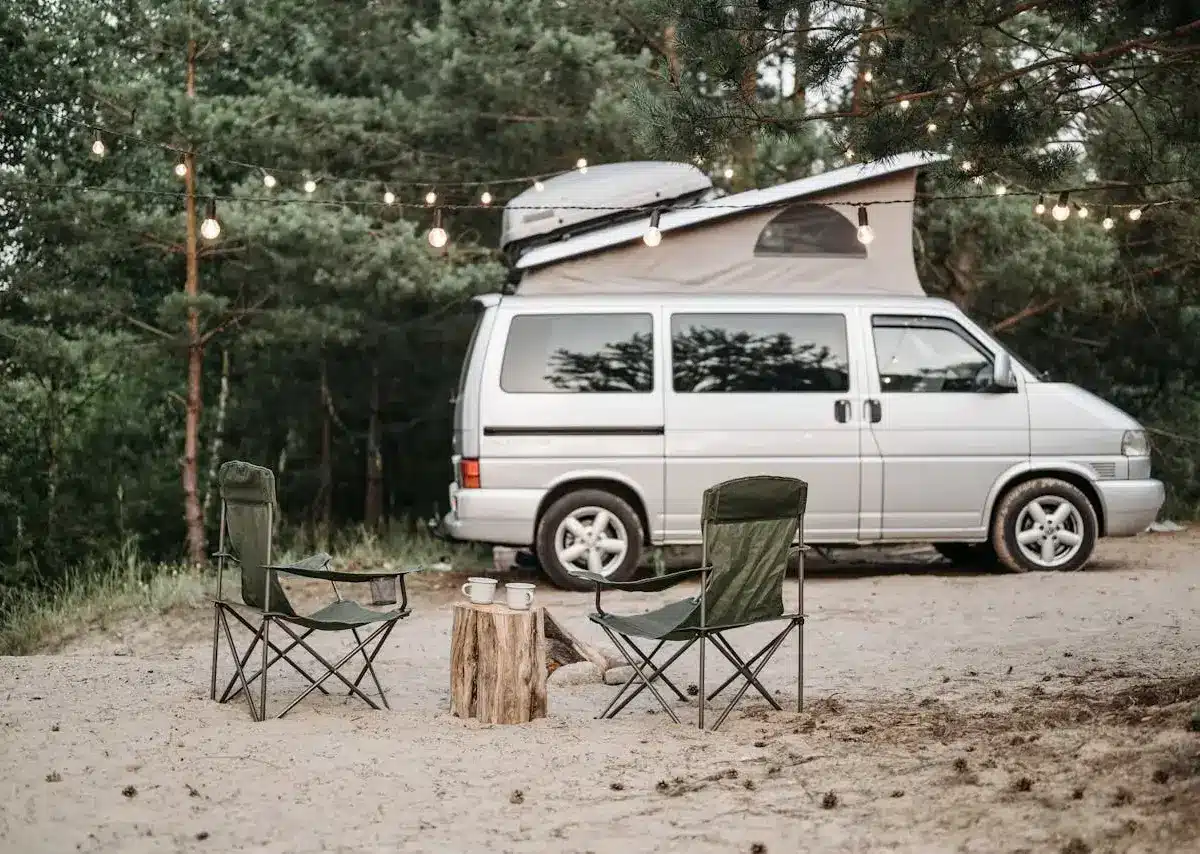 Camper van parked with chairs and string lights.