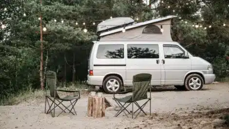Camper van parked with chairs and string lights.