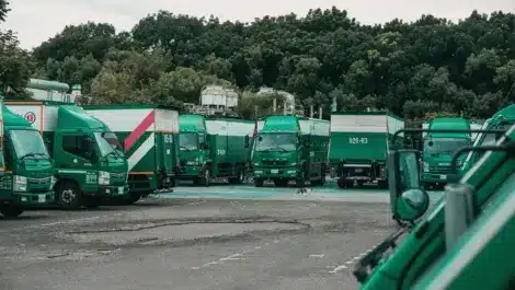 Fleet of green delivery trucks parked in a lot with trees in the background.