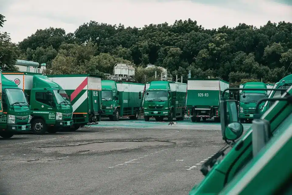 Fleet of green delivery trucks parked in a lot with trees in the background.