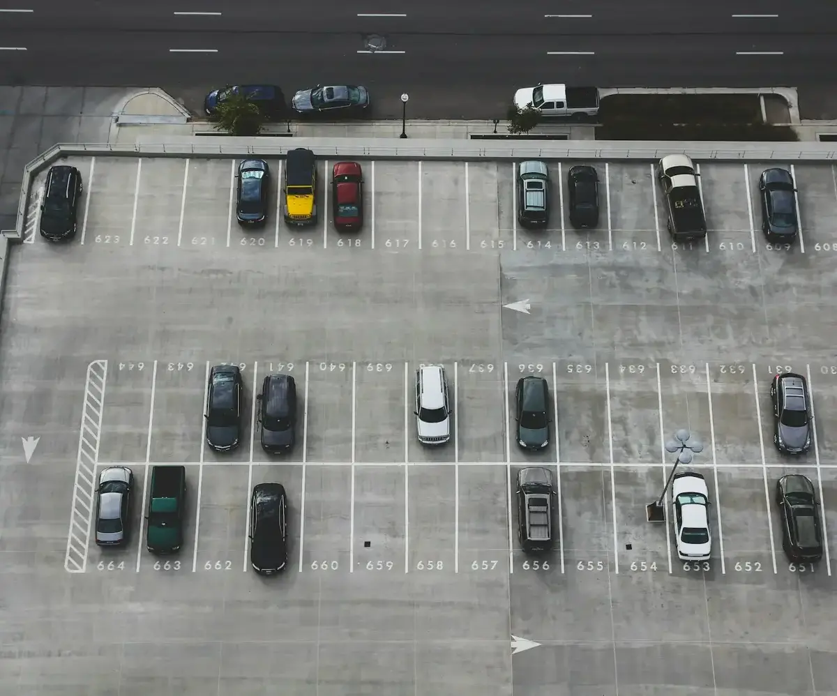 Top-down view of a parking lot with several parked cars near a main road.
