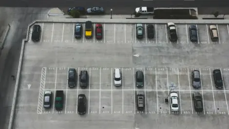 Top-down view of a parking lot with several parked cars near a main road.