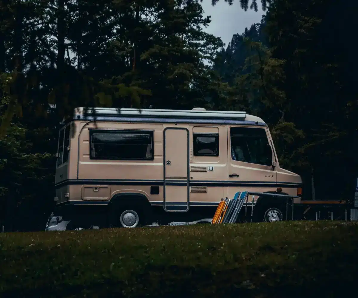 A beige motorhome parked in a forested area.