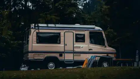 A beige motorhome parked in a forested area.
