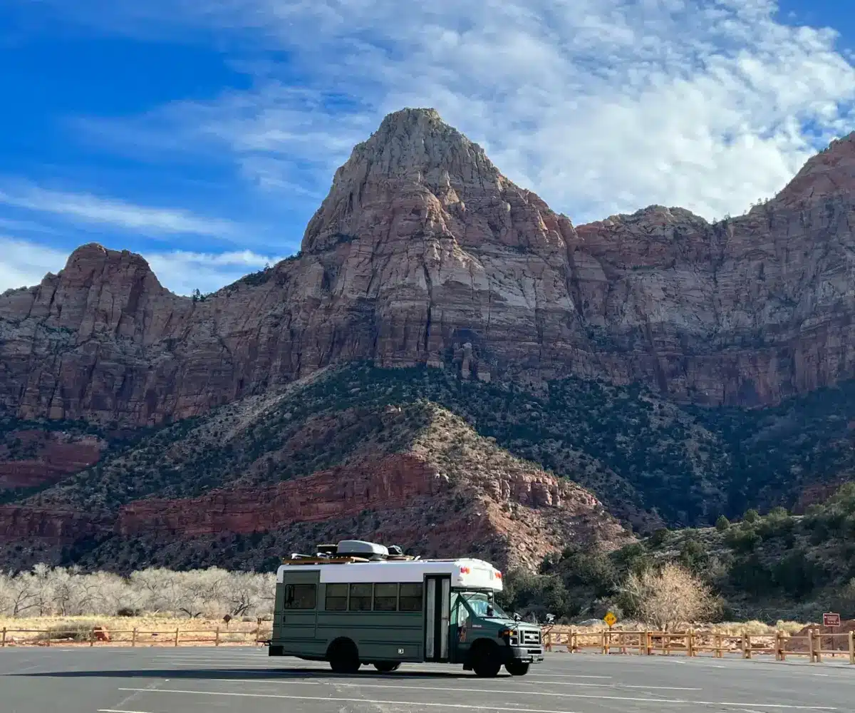 A camper van parked in front of towering red rock cliffs.