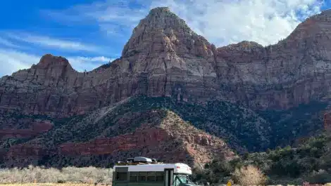 A camper van parked in front of towering red rock cliffs.