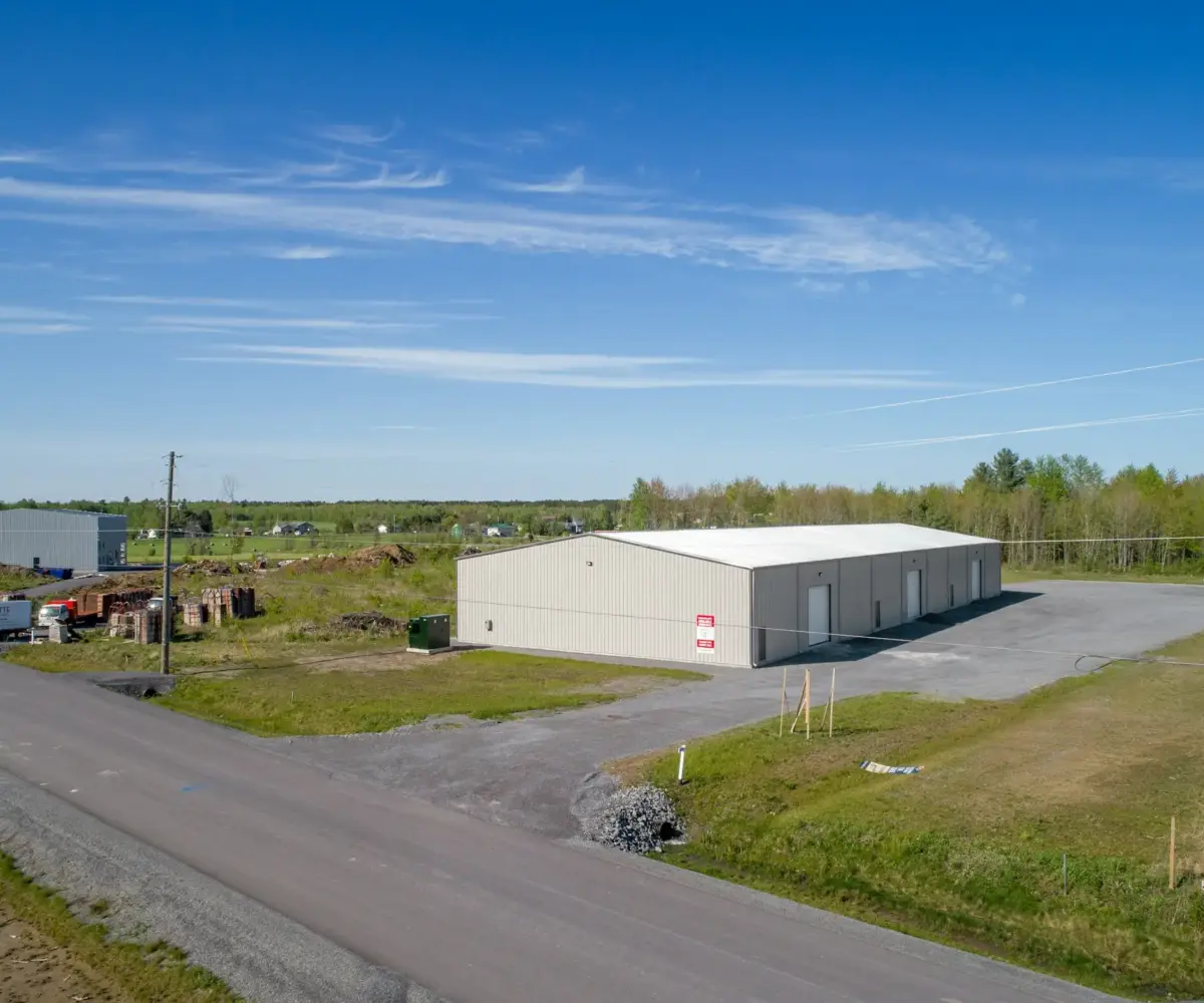 Metal building with outdoor storage space in a rural industrial area under clear blue sky.