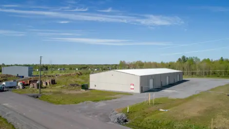 Metal building with outdoor storage space in a rural industrial area under clear blue sky.