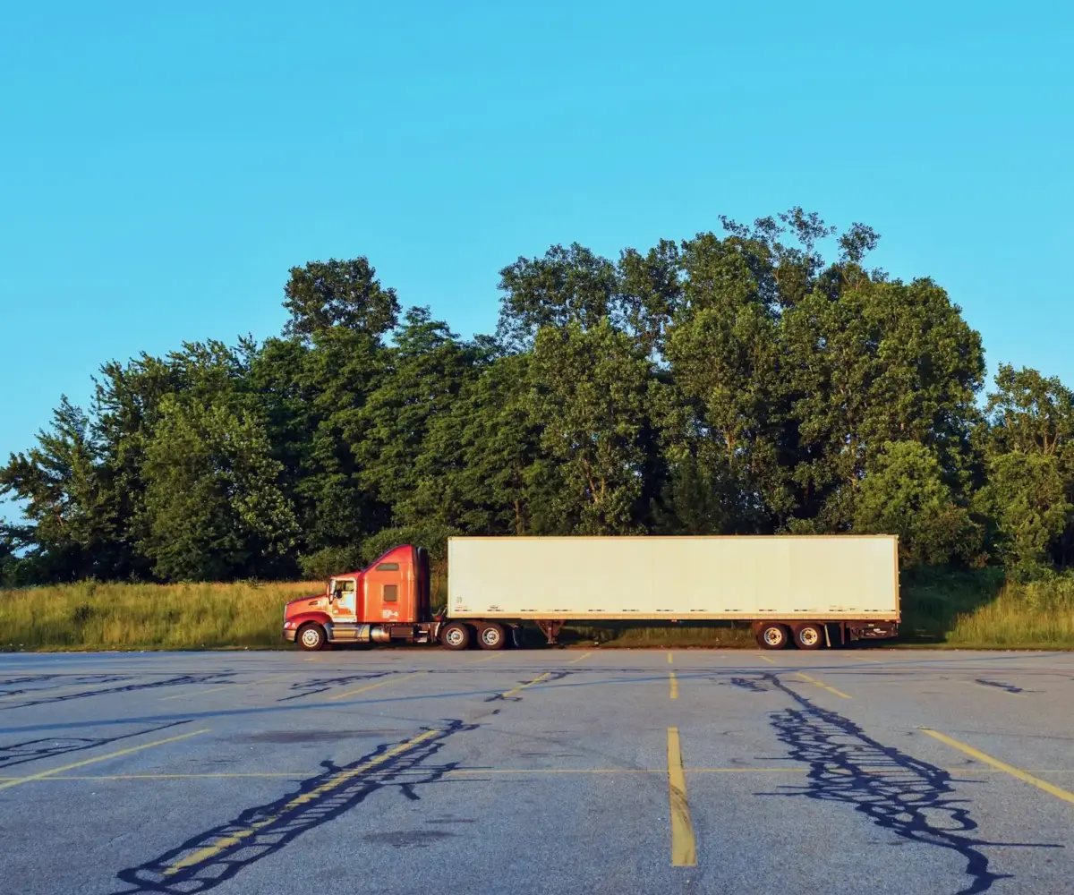 Red semi-truck with a white trailer parked alone in an empty lot.