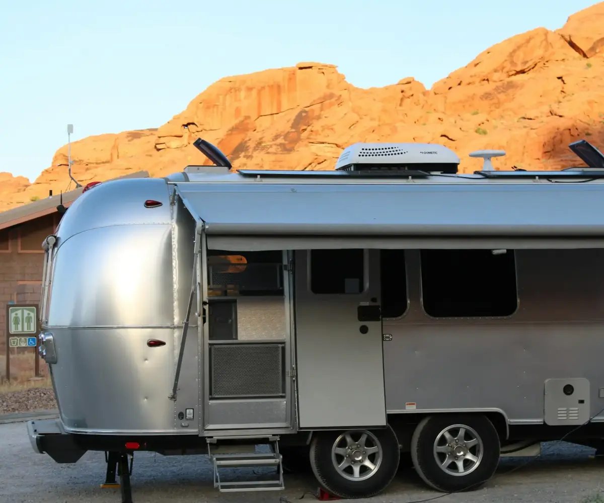Silver Airstream trailer parked near red rock cliffs and rest area building.