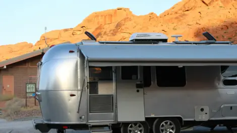 Silver Airstream trailer parked near red rock cliffs and rest area building.