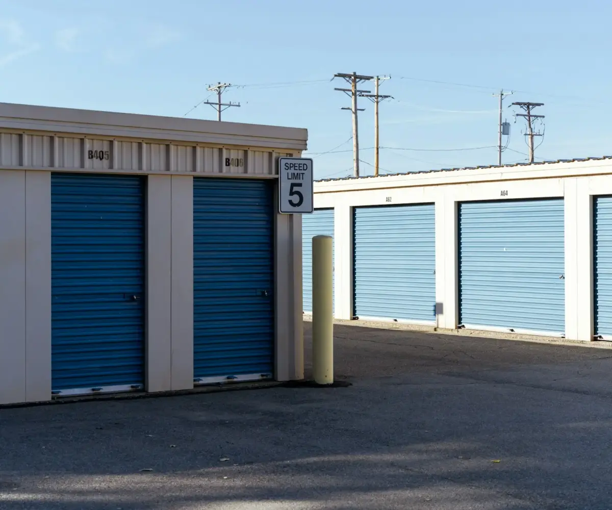 Outdoor self-storage facility with blue roll-up doors and a speed limit sign.