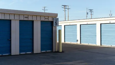 Outdoor self-storage facility with blue roll-up doors and a speed limit sign.