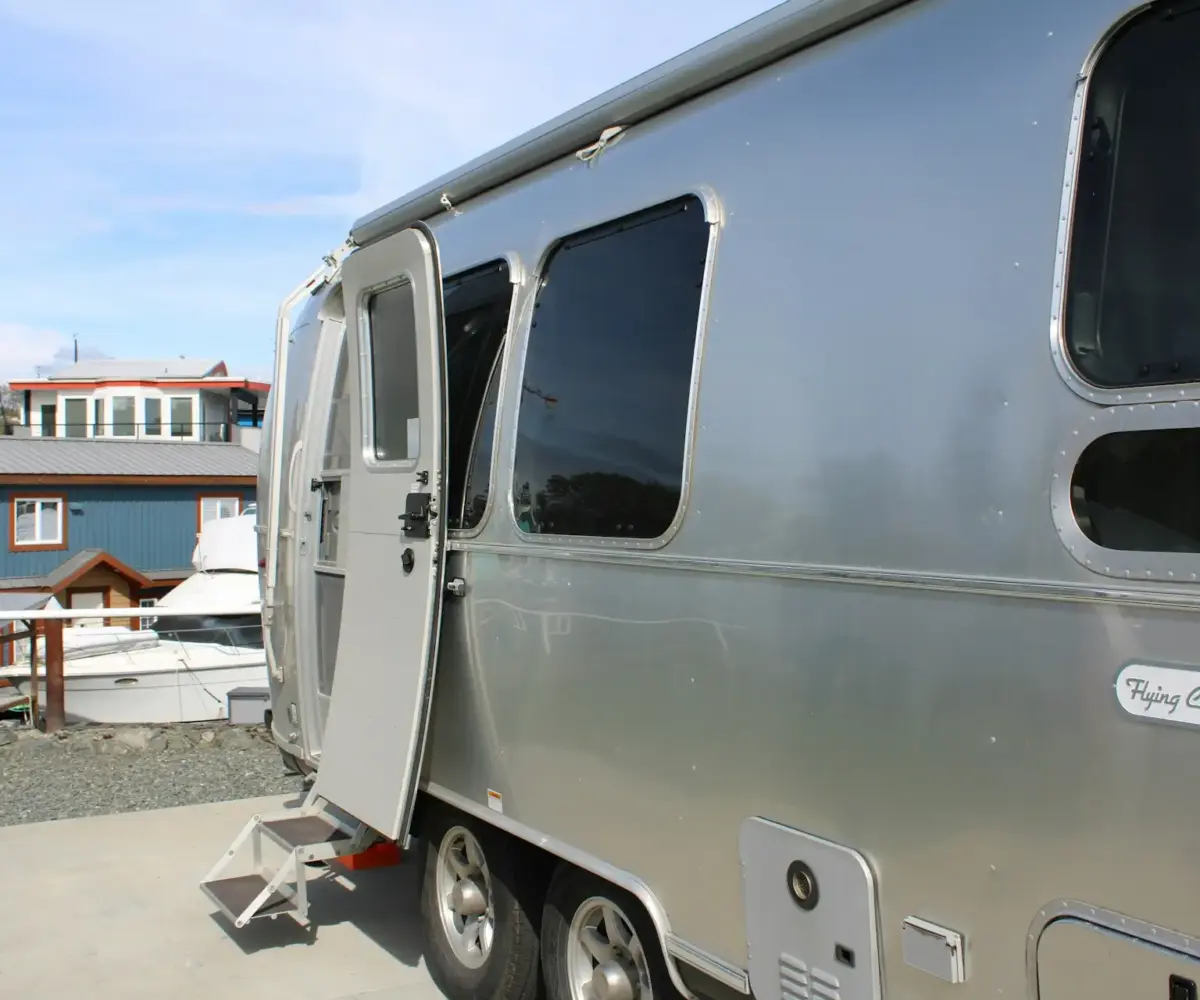 Silver Airstream trailer with open door parked near boats and houses.