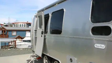 Silver Airstream trailer with open door parked near boats and houses.