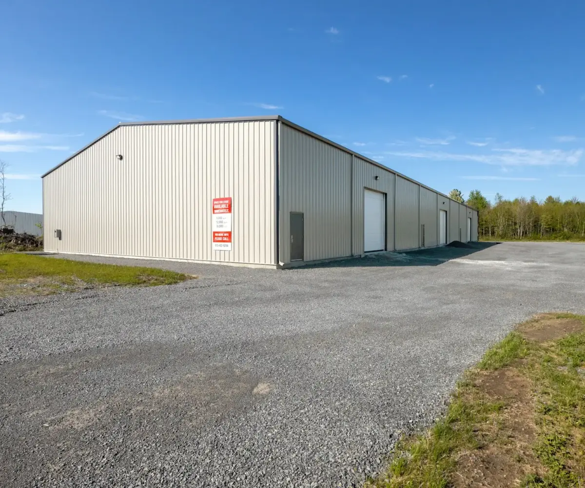 Industrial storage warehouse with roll-up doors and gravel yard under clear sky.