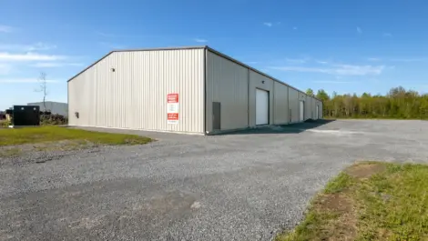 Industrial storage warehouse with roll-up doors and gravel yard under clear sky.