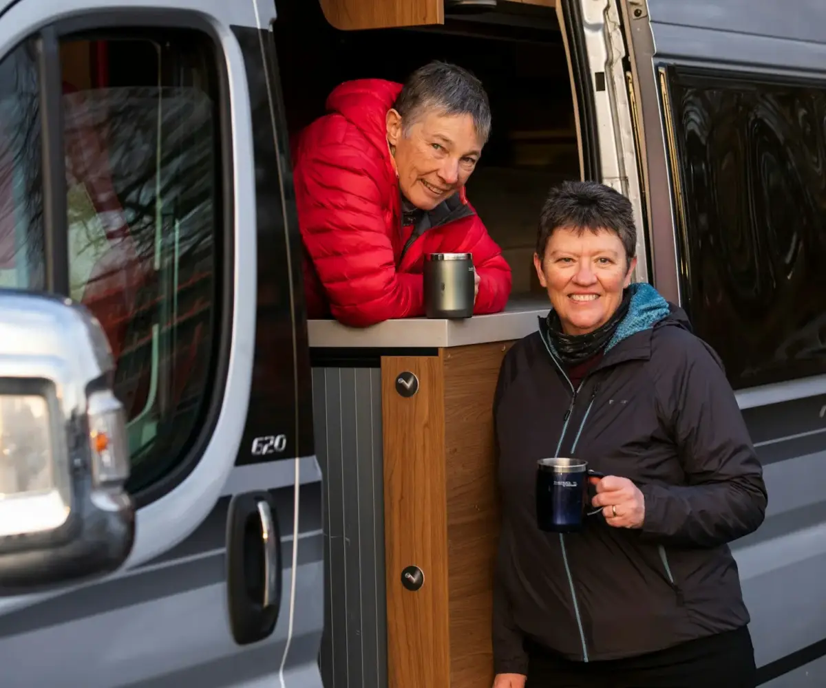 Two women enjoying coffee outside their motorhome.