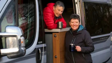 Two women enjoying coffee outside their motorhome.