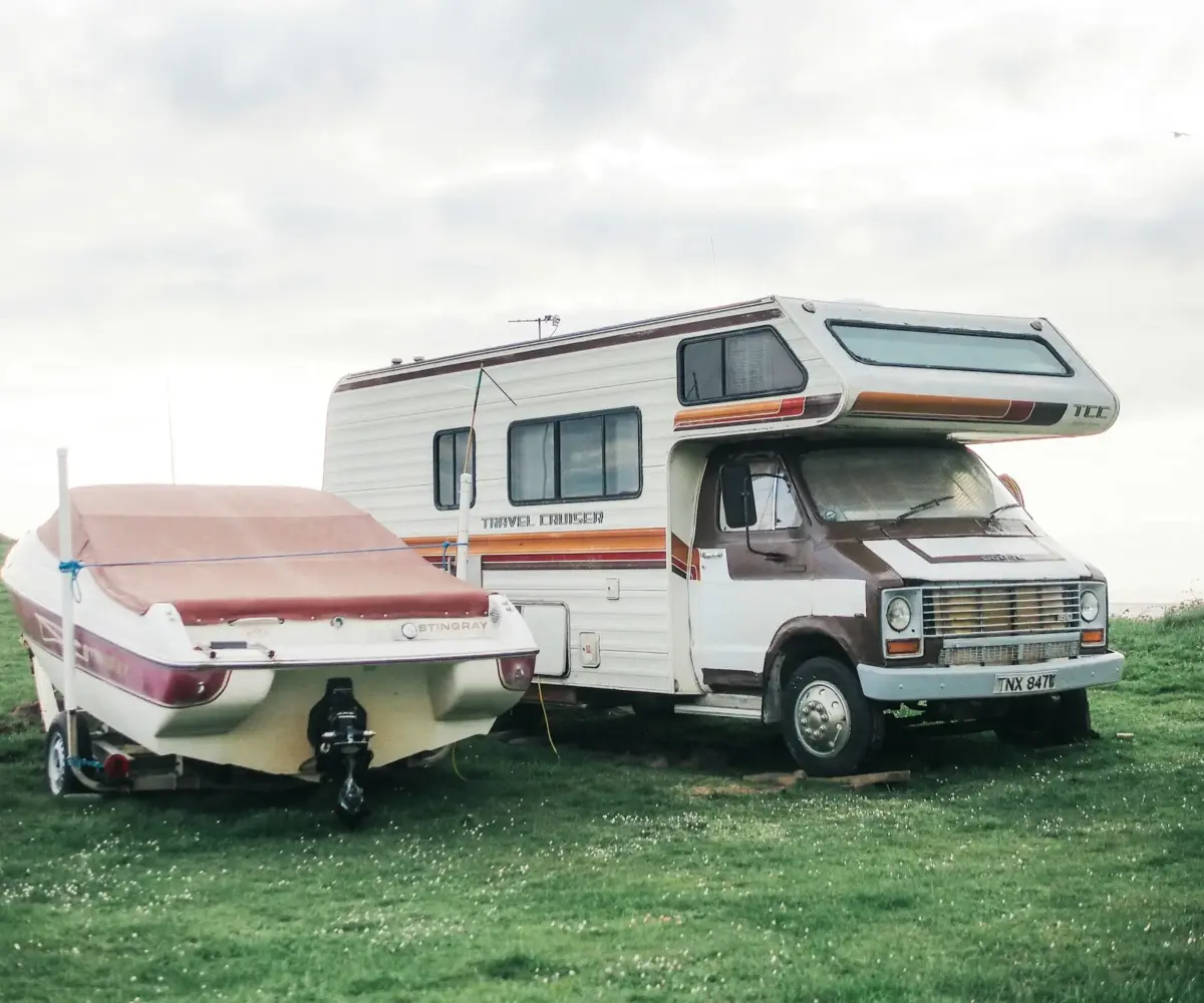 Vintage RV parked beside a covered Stingray boat on a grassy field.