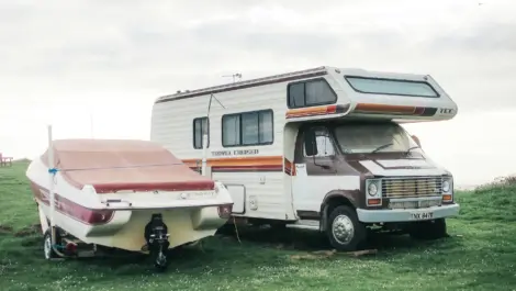 Vintage RV parked beside a covered Stingray boat on a grassy field.