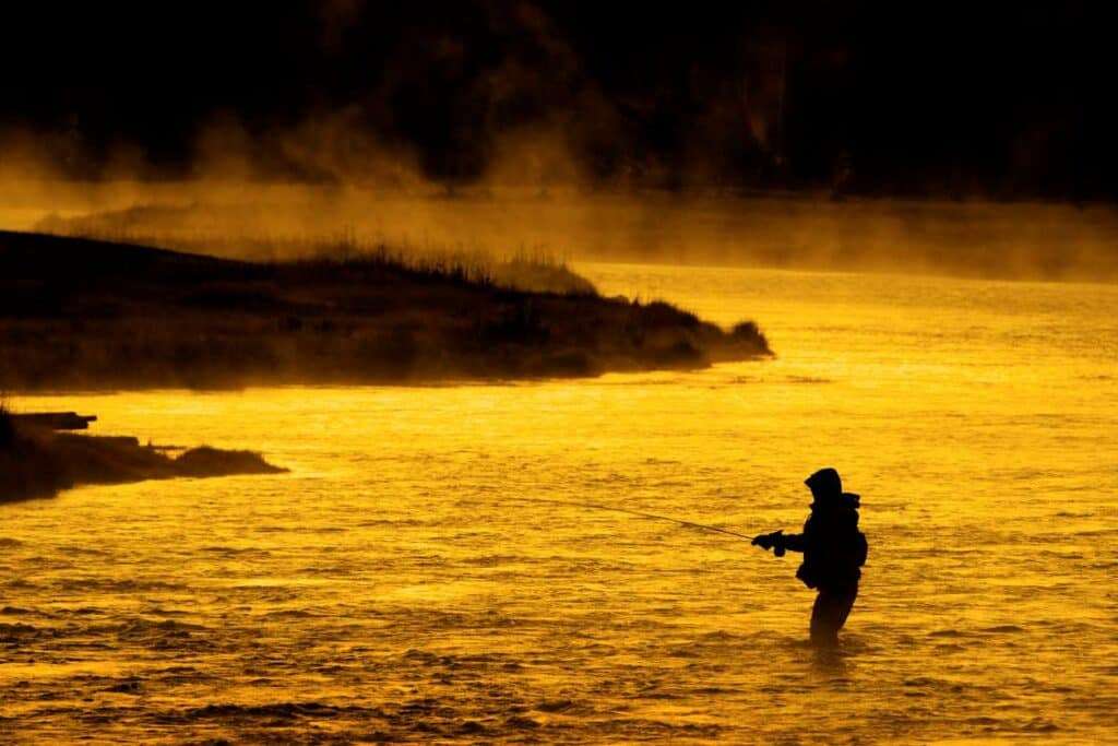 The silhouette of an angler fly-fishing during sunset.