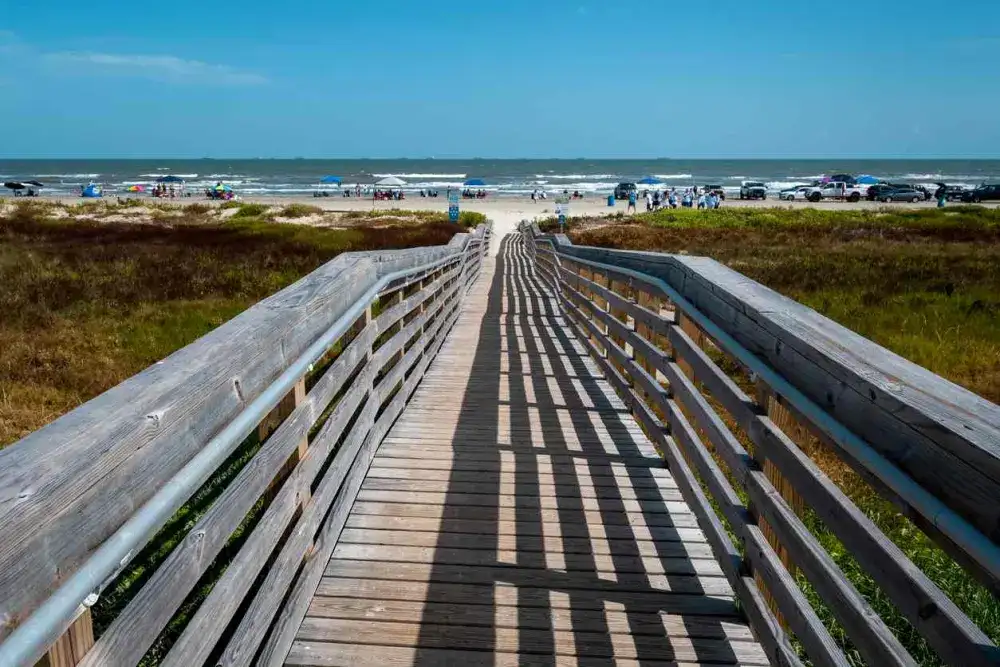 Boardwalk leading to the beach, which has many tents, cars, and visitors.