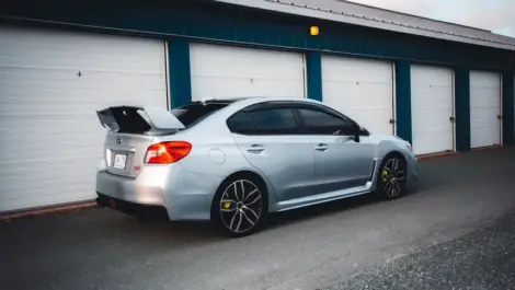 Silver sedan parked outside an enclosed car storage unit.