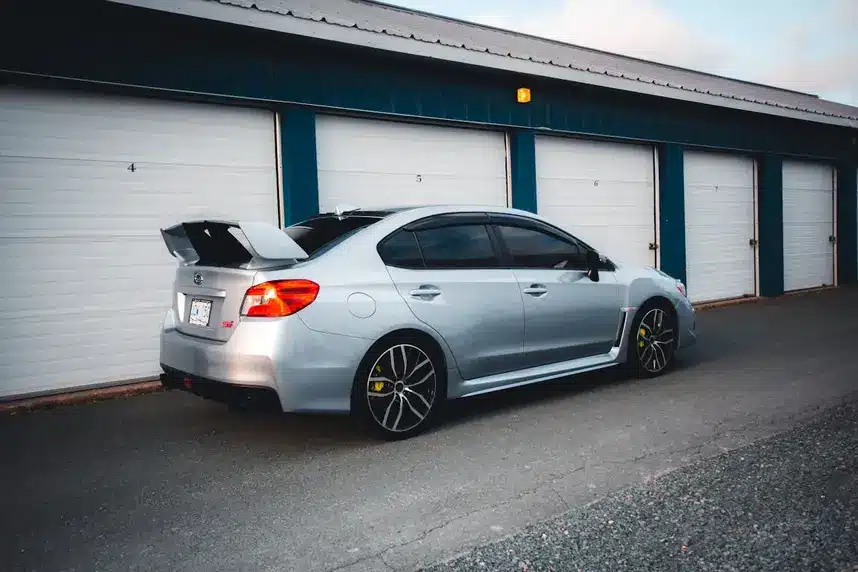 Silver sedan parked outside an enclosed car storage unit.